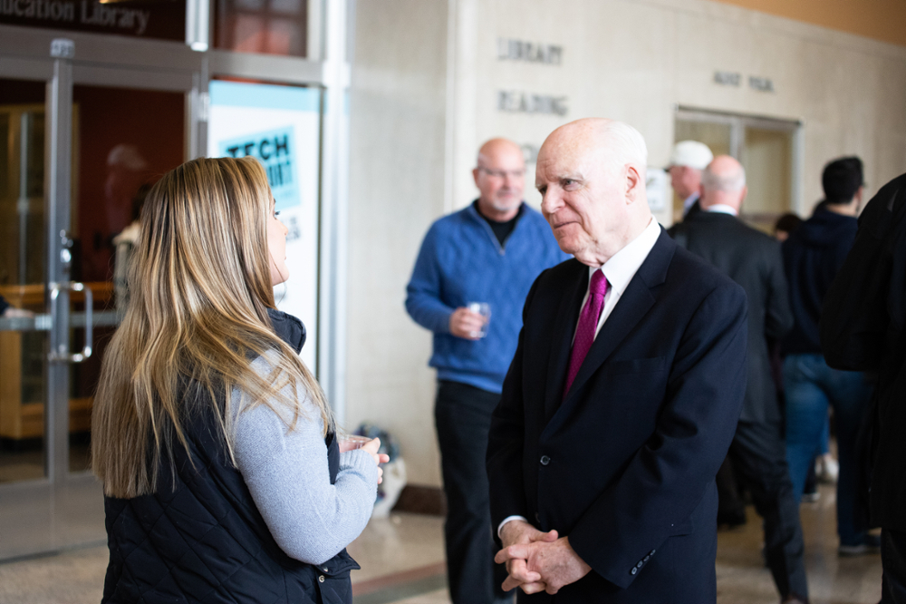 Brian listens intently to a student whose back is to camera. He's smiling. They're at a reception in the lobby outside of Loeb Playhouse on Purdue's campus.