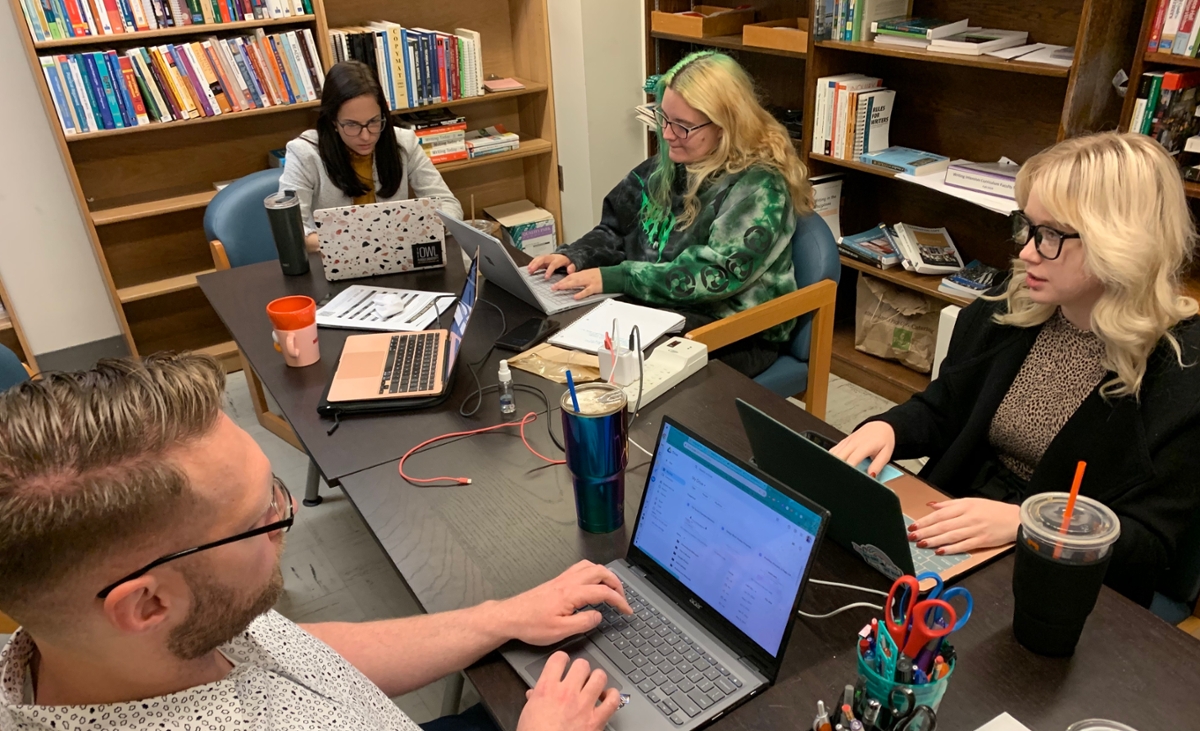 Group of graduate students working with laptops on wooden table.