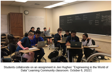 students sit together in pairs and work together on laptops in a classroom