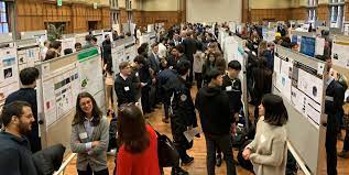 photograph of the undergraduate research conference at Purdue. Many students and faculty gather around several research posters.