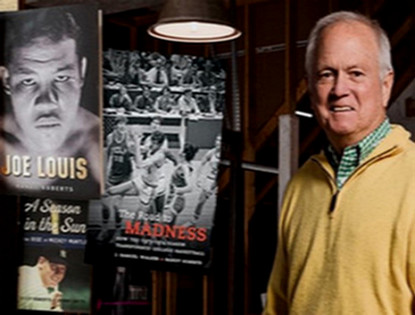 Randy Roberts stands beside displays of his sports history books, including titles on Joe Louis and basketball, highlighting his scholarly work.