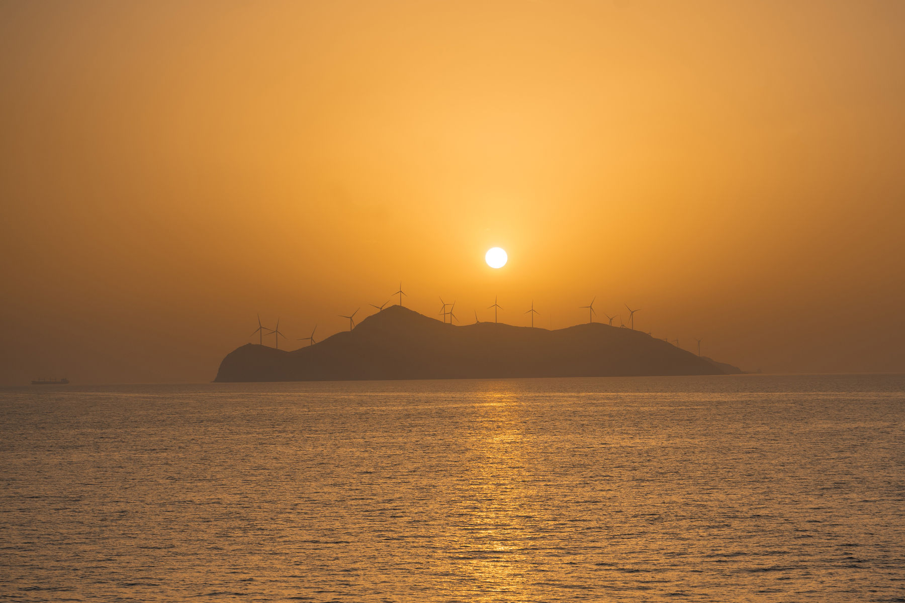 Sunset over a distant island, with the silhouette of multiple windmills.