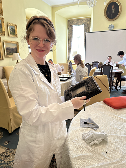 student in white labcoat in archive holding artifact