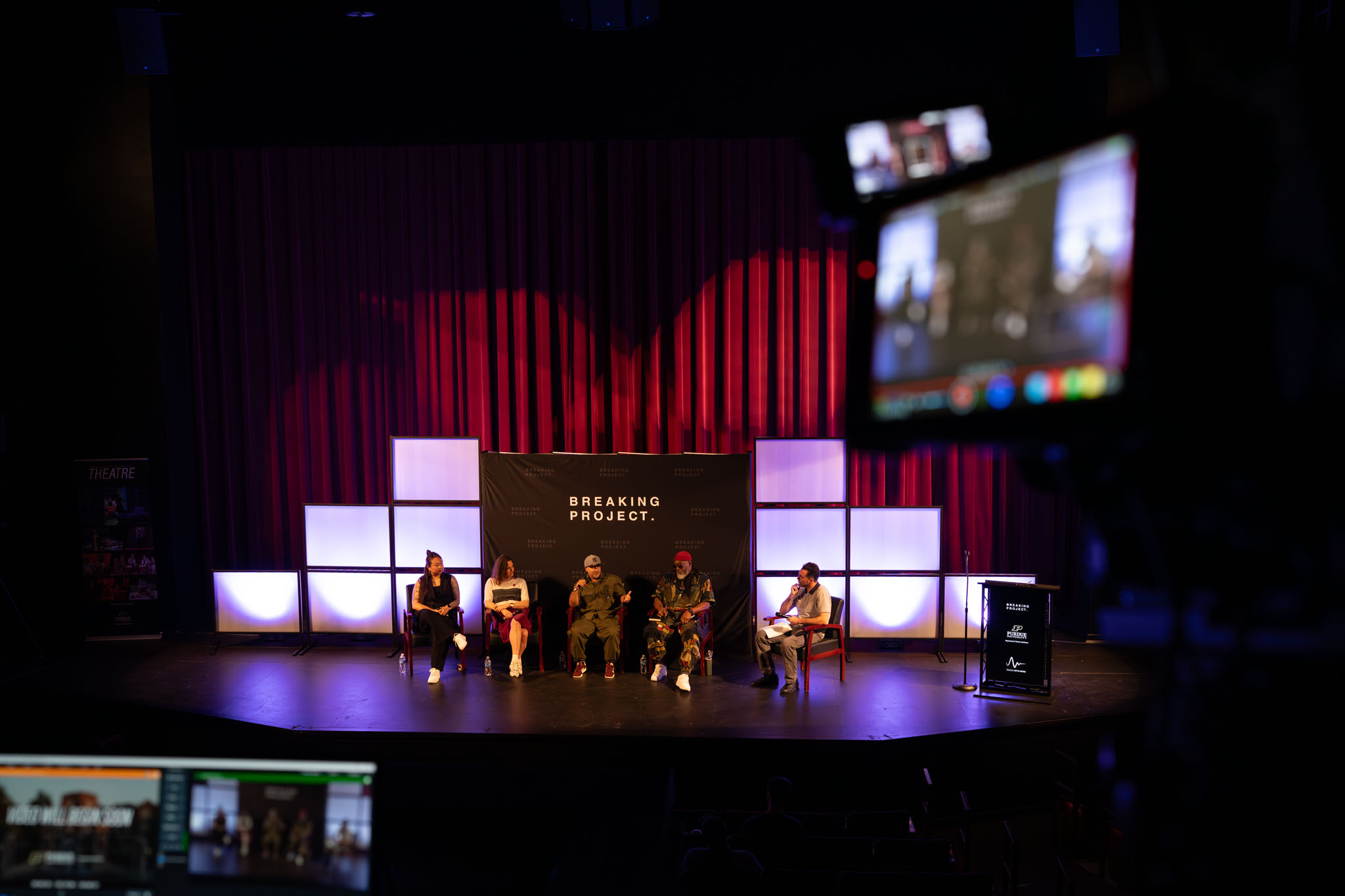 A panel of artists on a stage in front of a backdrop that reads "Breaking Project."
