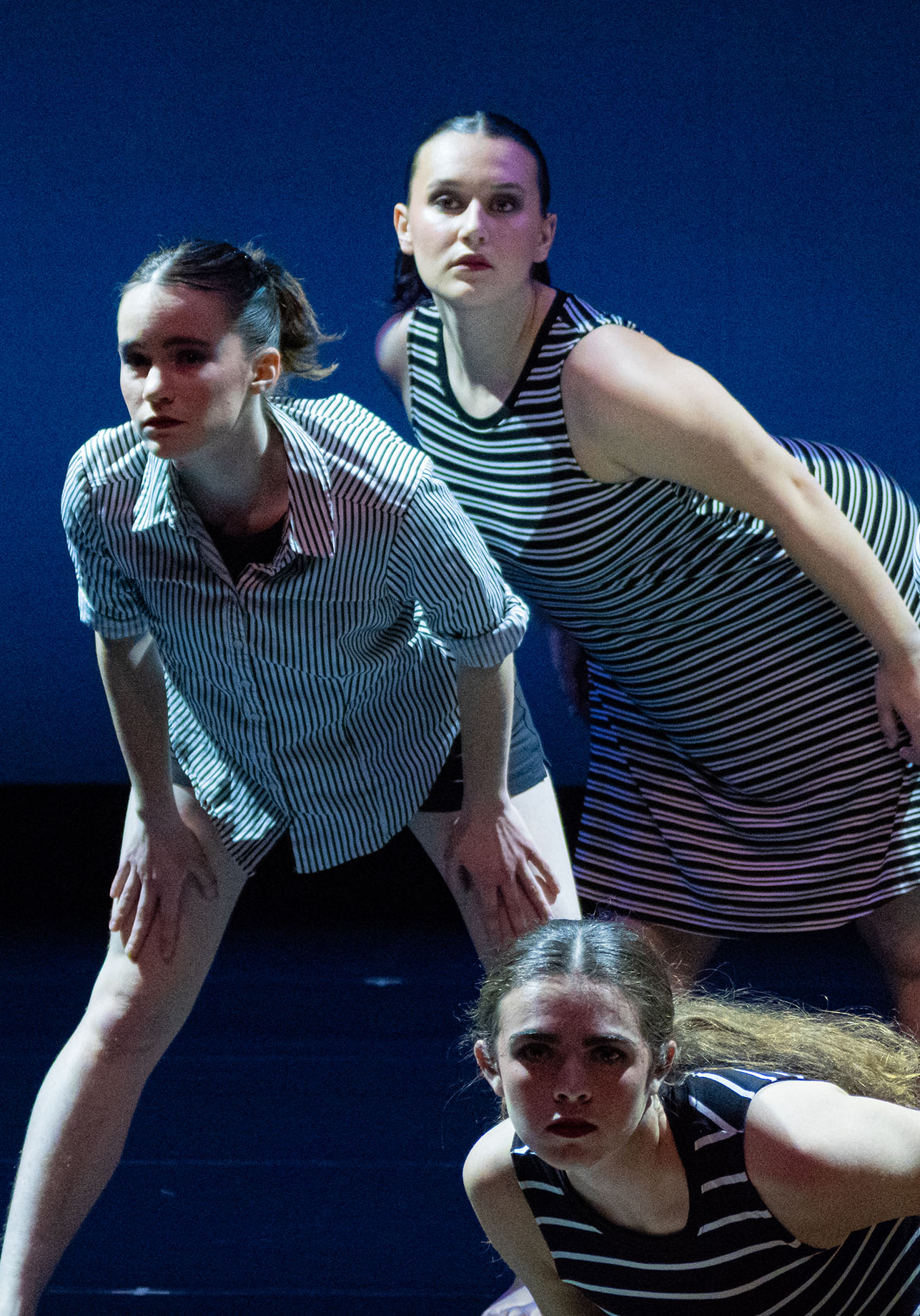 Three dancers in front of a blue background looking with curiosity into the audience.