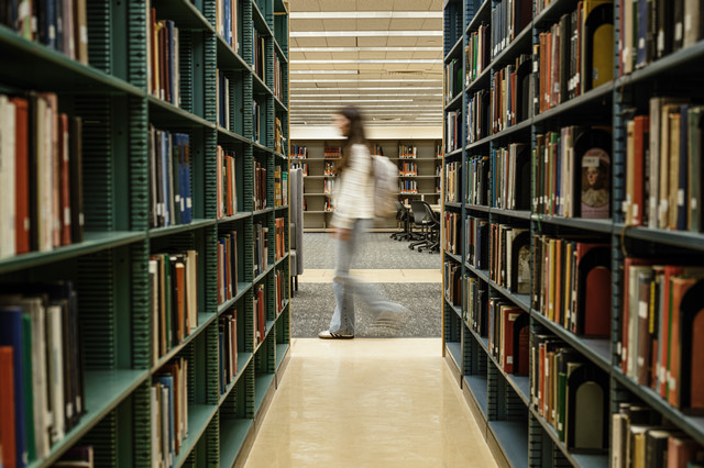 photo in the library with books and blurred picture of student walking