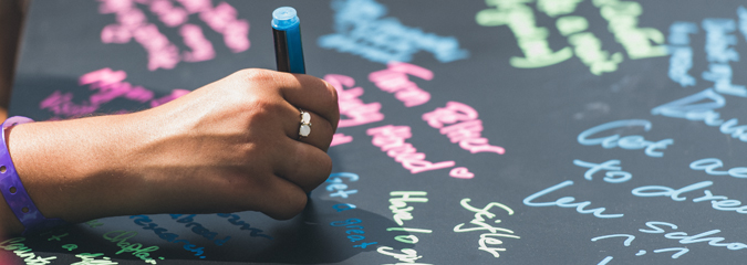 Closeup of a hand writing on a chalkboard.