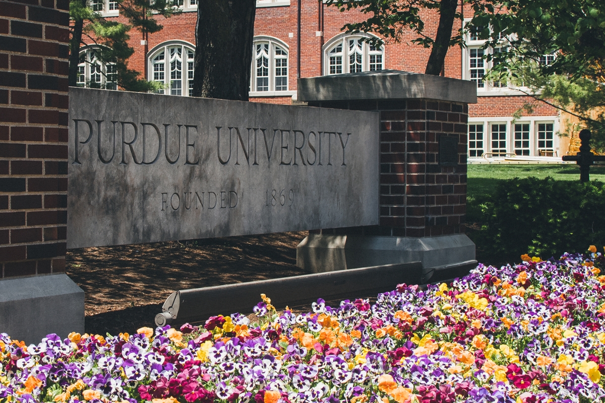 Brick Purdue University sign with flowers around it.