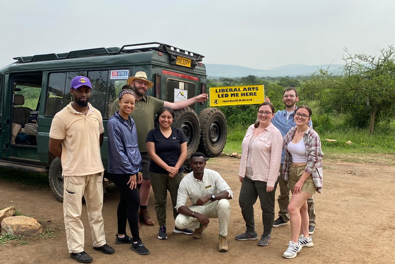 The CLA Study Abroad team in Akagera National Park, holding a sign that says "Liberal Arts Led Me Here".