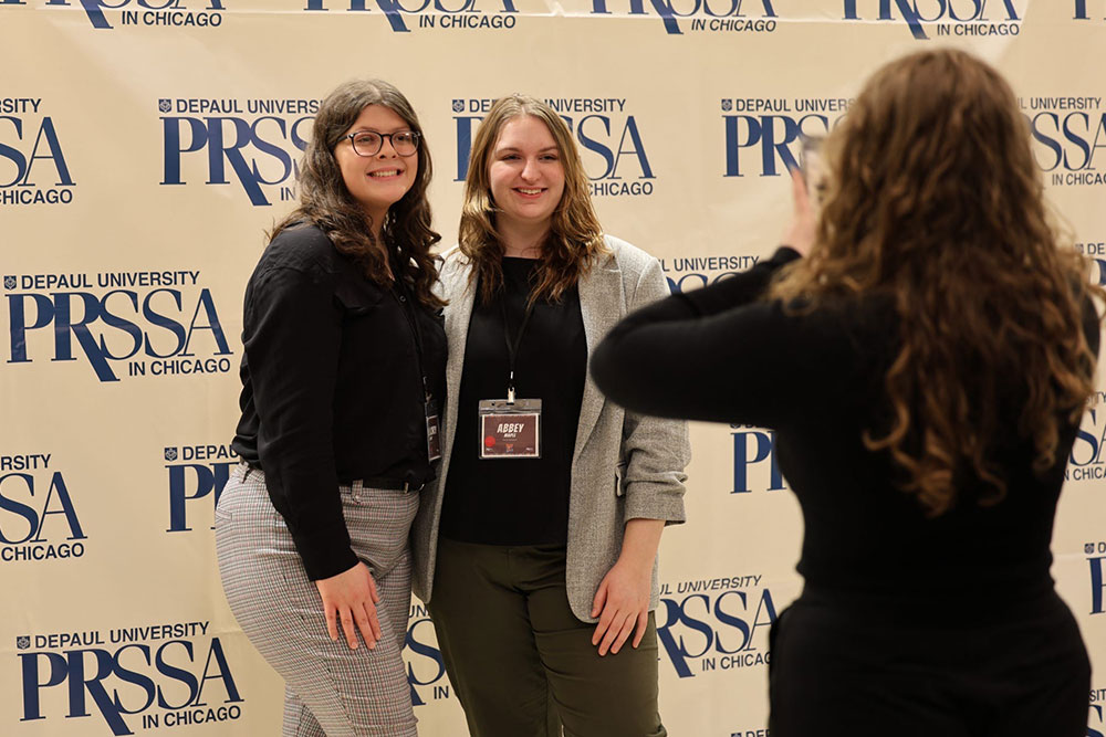 Abbey and another conference attendee standing in front of a PRSSA photo background posing for a picture.