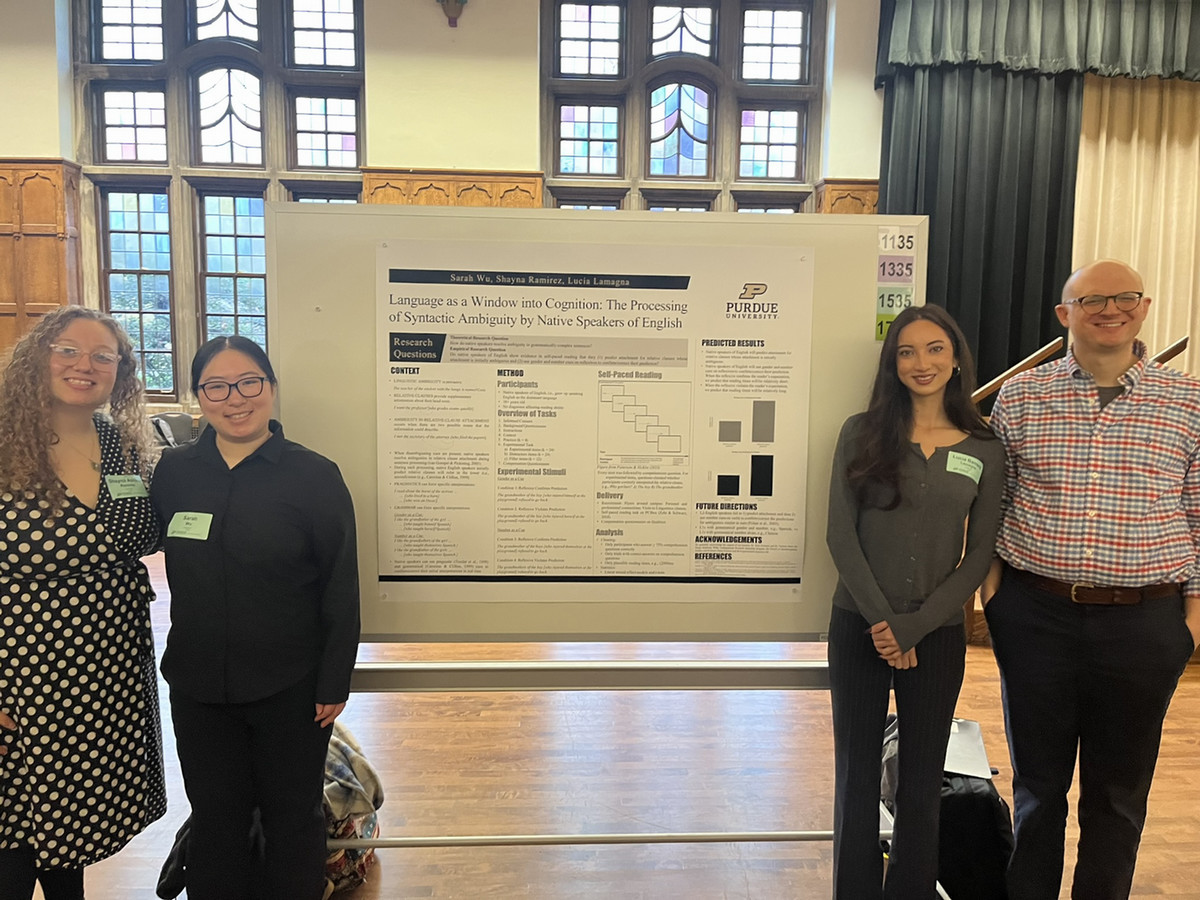 Purdue students and their professor standing by a poster that displays some data about their research