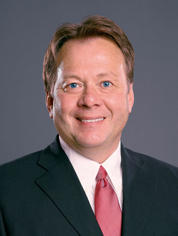 Chuck Jones wearing a suit and red tie for a headshot.
