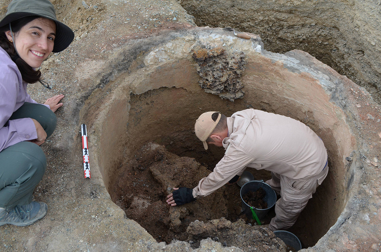 Two people digging into an ancient furnace.