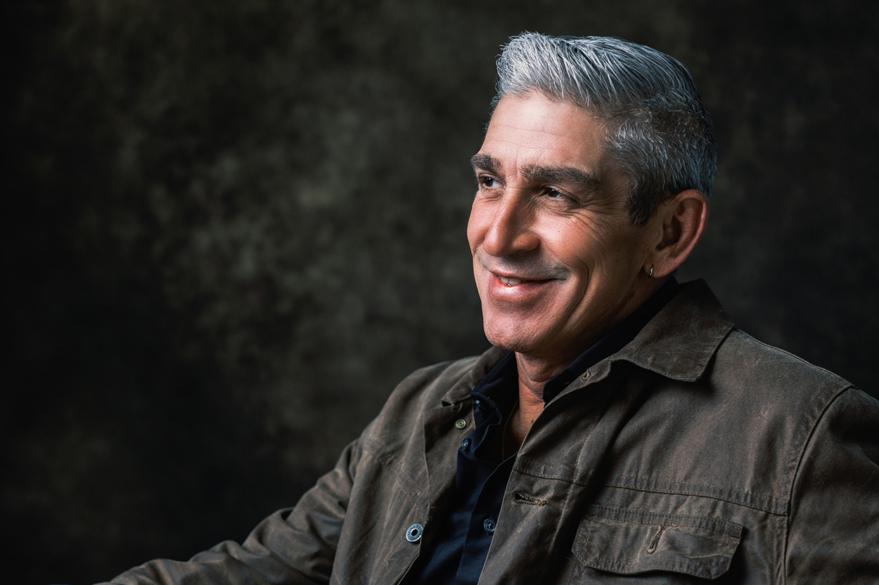 Richard posing on a stool in front of a gray background.