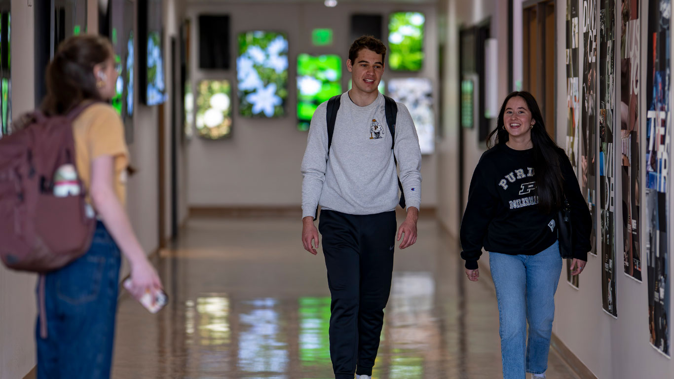 Three Purdue students in a hallway with two walking toward the camera