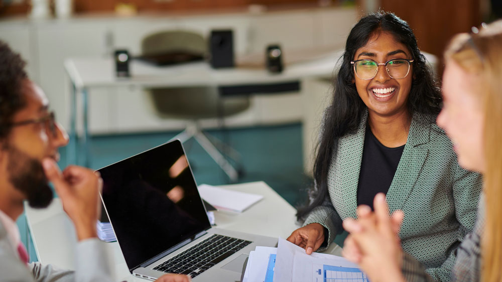 Three students talking with one looking at a computer screen