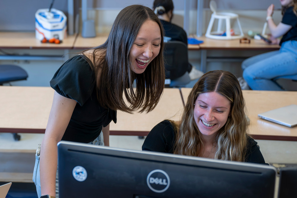 Two Purdue University students smiling while looking at a laptop computer working on a project